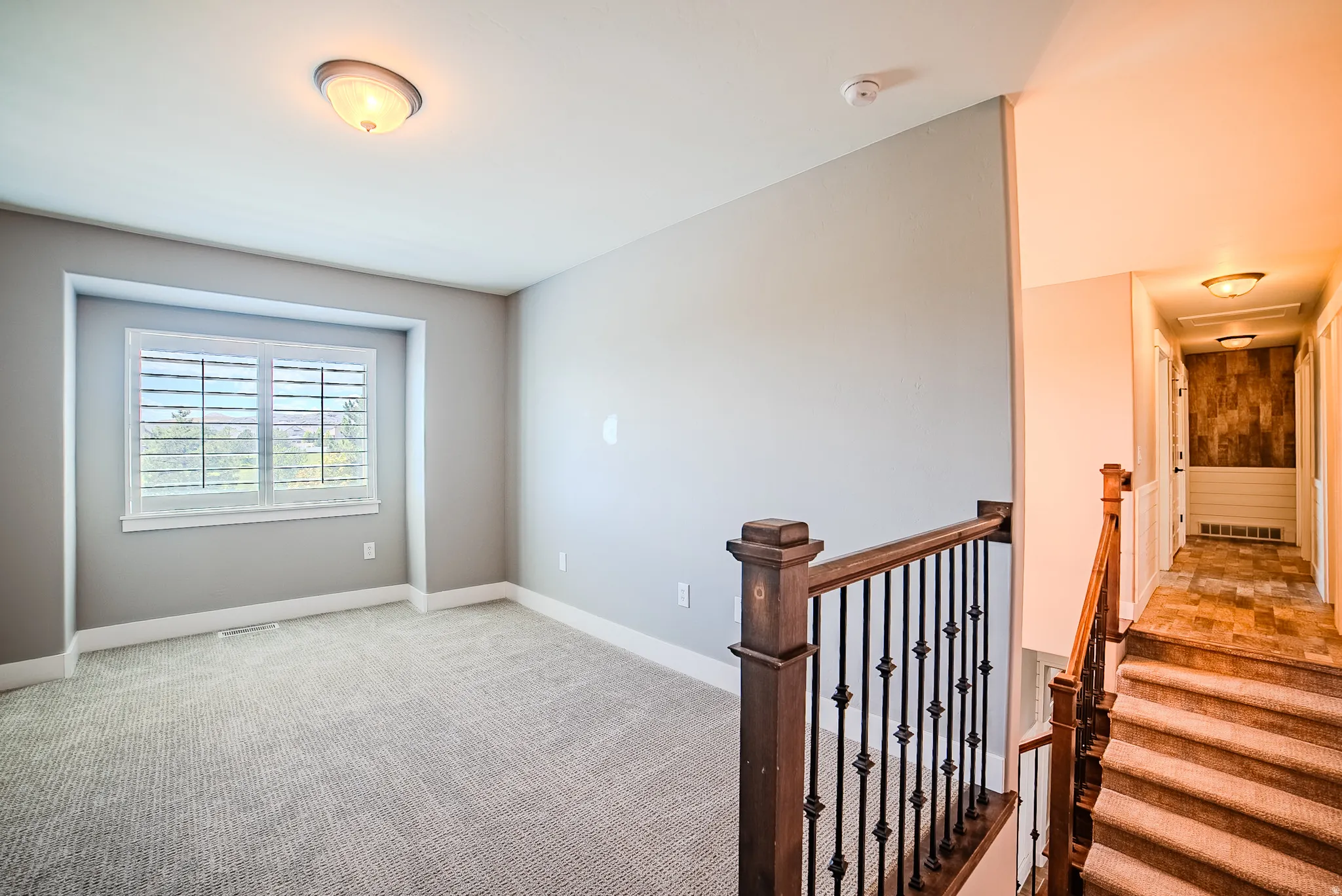 Upper-level room featuring plush carpeting, a large window with white blinds, and ceiling-mounted lighting