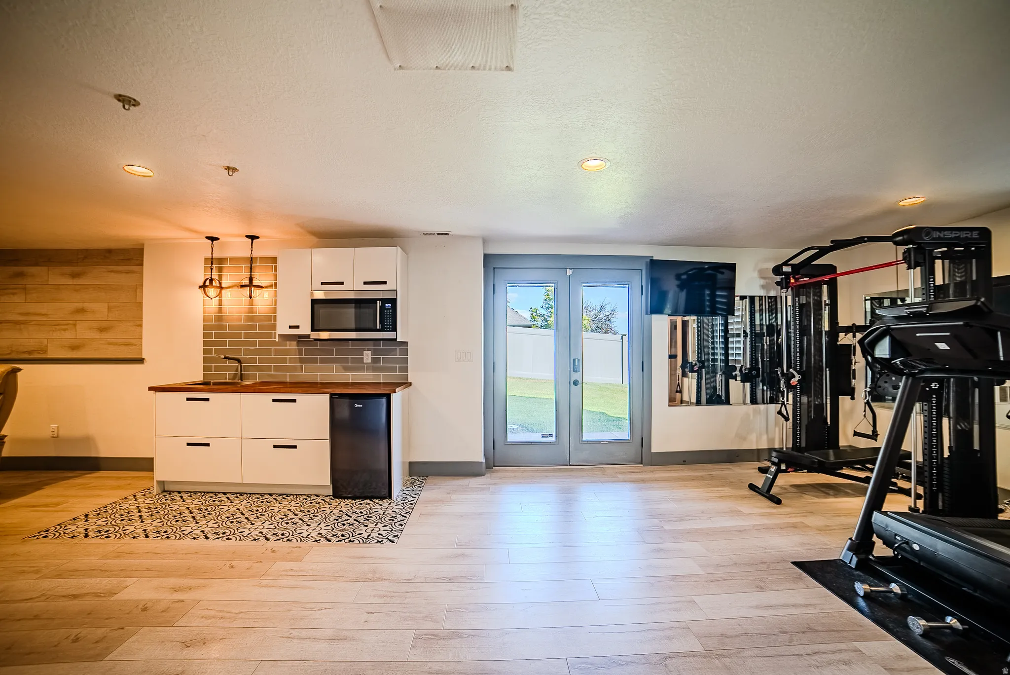 Spacious room featuring light wood-finish flooring and a contemporary kitchenette with white cabinetry, wood countertops, and a subway tile backsplash