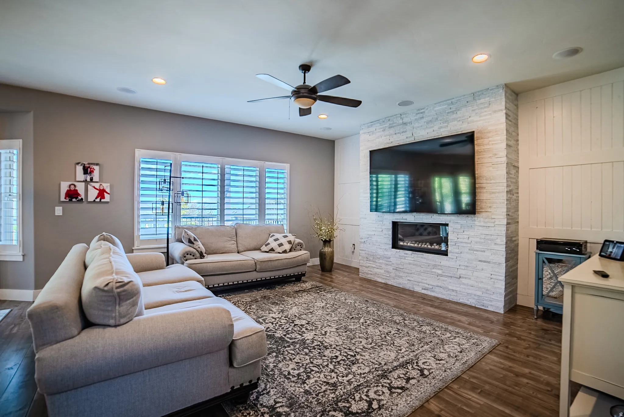 Living area featuring a textured stone fireplace surround with an integrated linear fireplace, wood-finish flooring, recessed lighting, and a ceiling fan