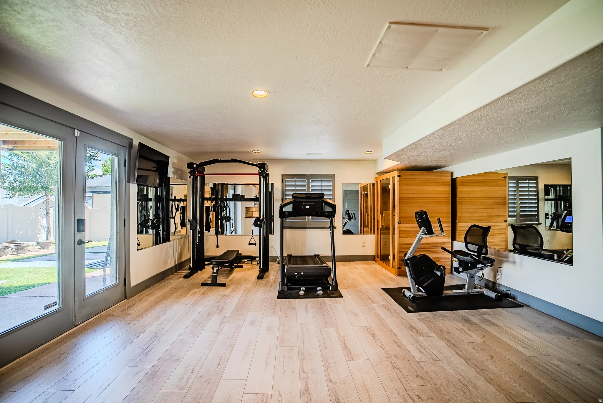 Spacious interior room featuring wood-finish flooring, recessed lighting, and wall-mounted mirrors