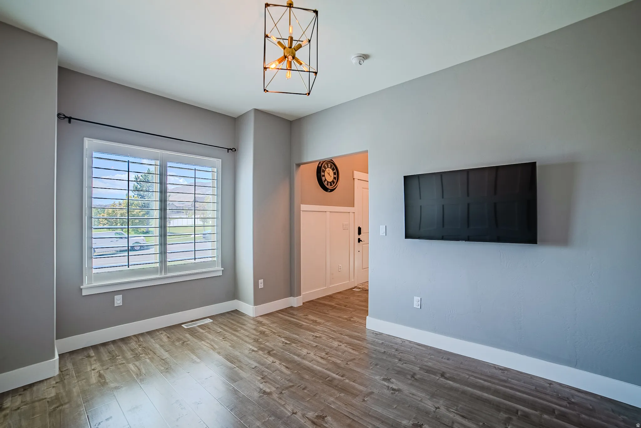 Open concept interior featuring wood-finish flooring, a contemporary cage chandelier, and a large window with white louvered blinds
