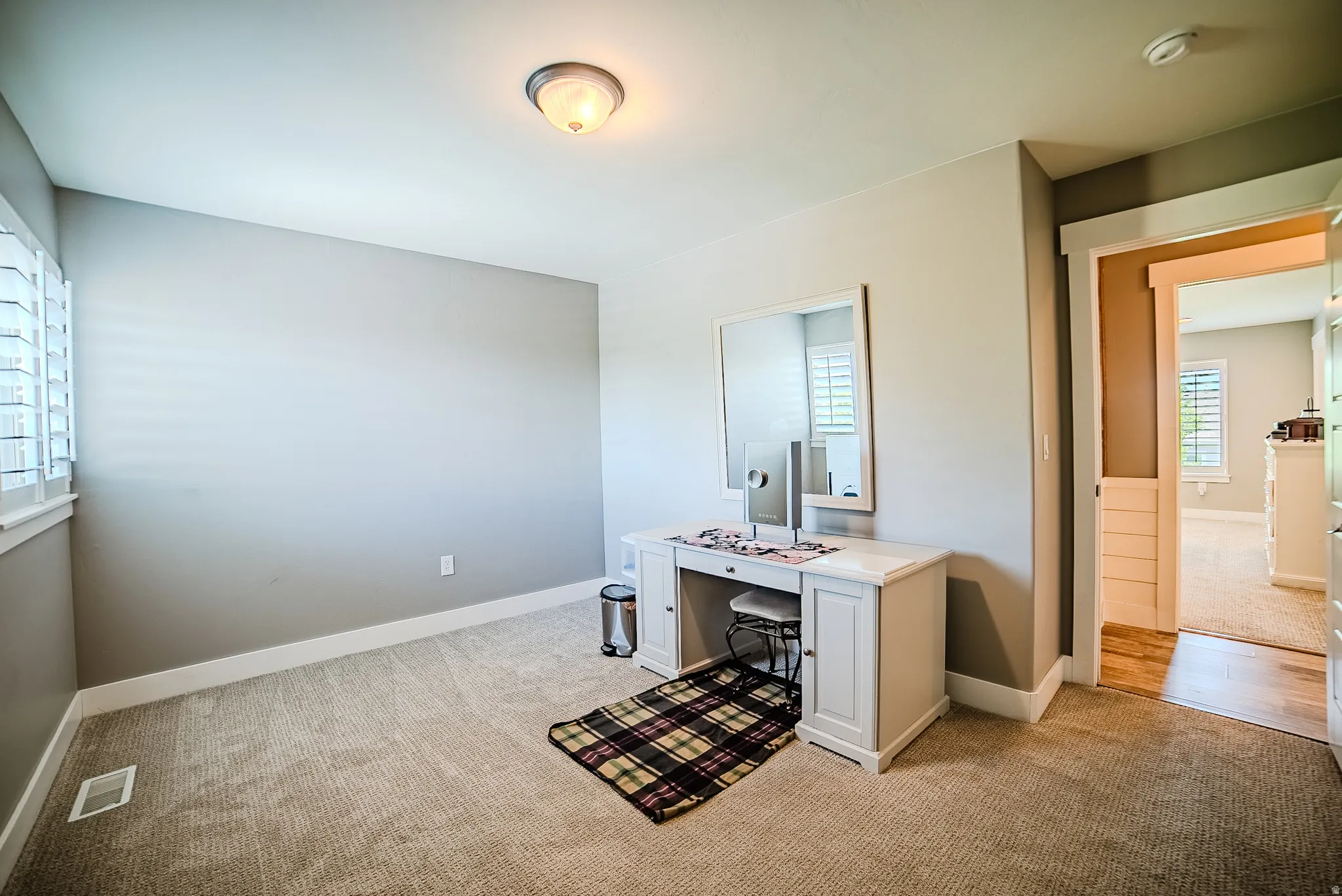 Carpeted room featuring a window with plantation shutters, neutral wall paint, white baseboards, and an overhead flush-mount light fixture