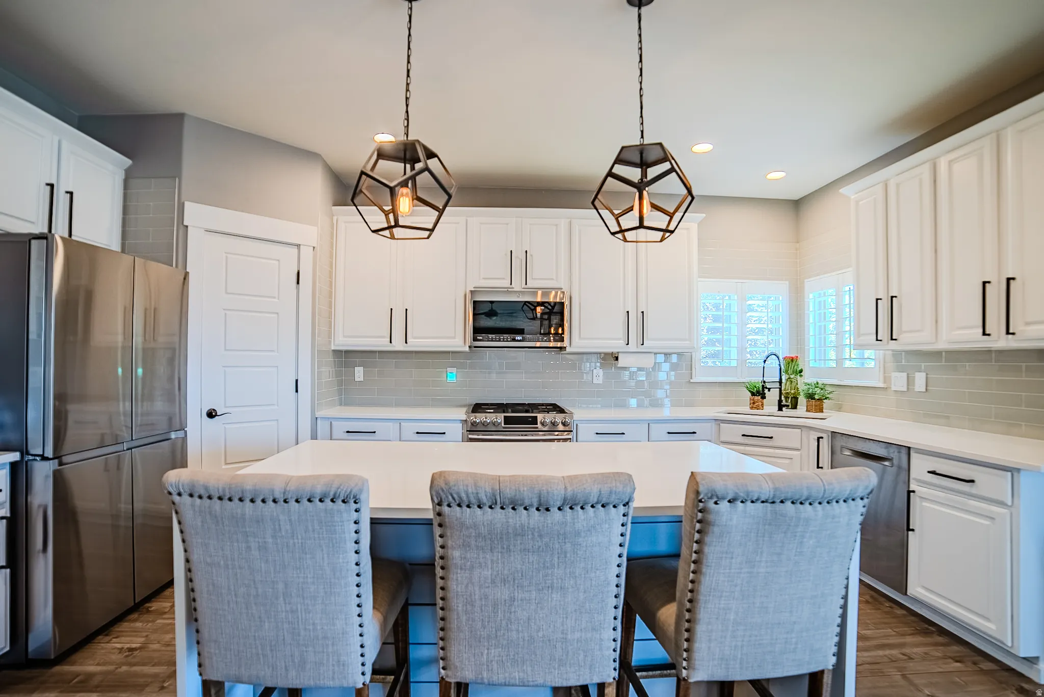 Kitchen featuring a central island, white cabinetry, stainless steel appliances, geometric pendant lighting, and light-toned backsplash tiling