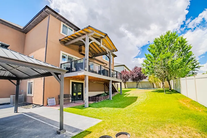 Spacious backyard featuring a covered patio, expansive lawn, mature trees, and a privacy fence