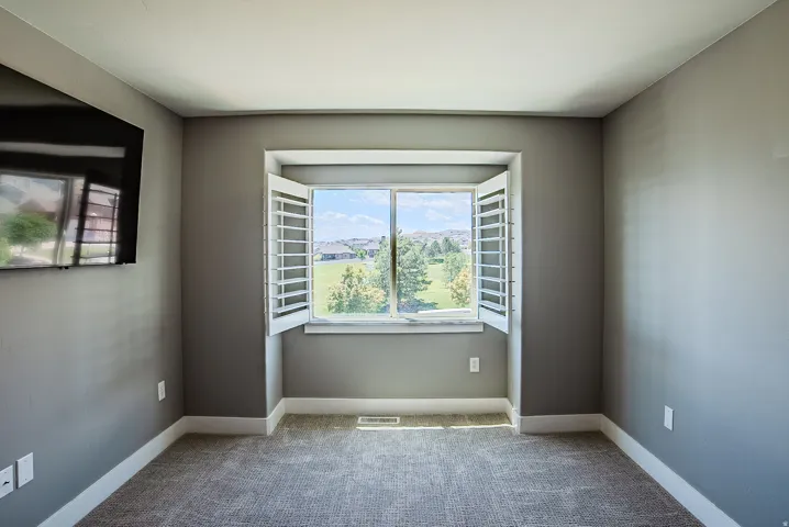 Recessed window with white plantation shutters, gray walls, white trim, and textured carpet flooring