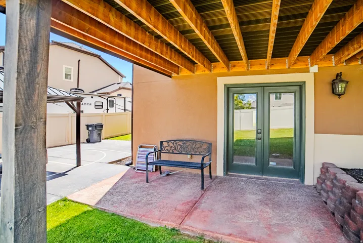 Covered patio featuring a concrete surface, exposed wood beam ceiling, and a dark green French door entry