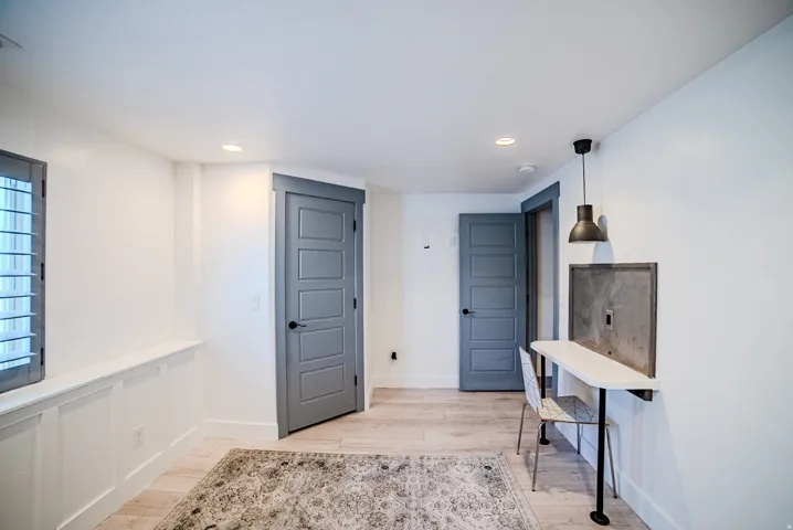 Room featuring light wood-finish flooring, two gray five-panel doors, recessed ceiling lighting, and a window with gray plantation shutters