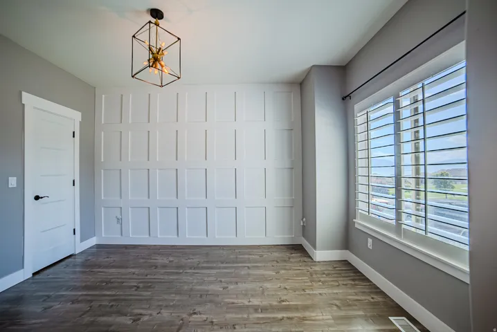 Feature wall with wainscoting detailing, wood-finish flooring, and a contemporary geometric chandelier