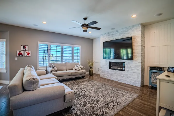 Living area featuring a textured stone fireplace surround with an integrated linear fireplace, wood-finish flooring, recessed lighting, and a ceiling fan