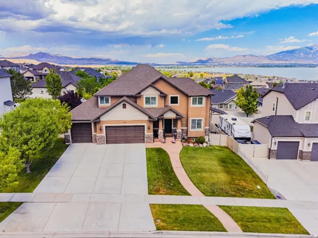 Two-story residence featuring a neutral stucco and stone facade, dual two-car garages, and a paved driveway