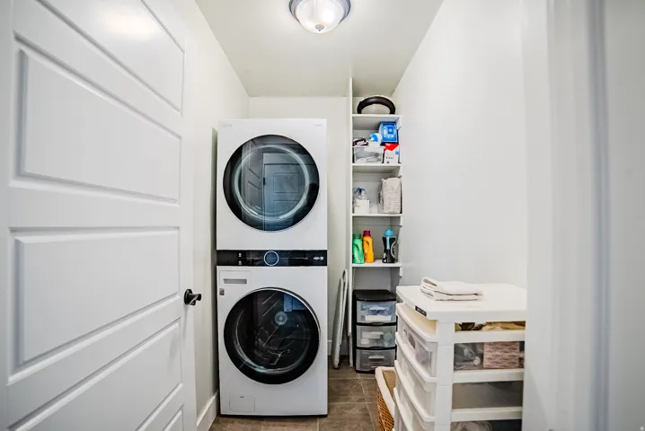 Dedicated laundry space featuring a stacked washer and dryer, recessed wall shelving, and tile flooring