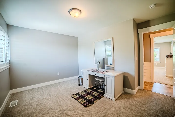 Carpeted room featuring a window with plantation shutters, neutral wall paint, white baseboards, and an overhead flush-mount light fixture