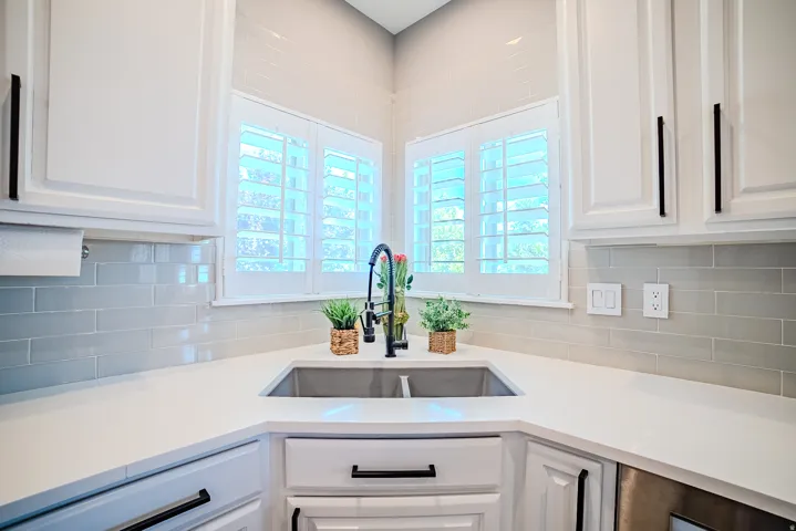 Corner kitchen sink with a matte black faucet, white shaker cabinetry with black bar pulls, light subway tile backsplash, and light-toned countertops
