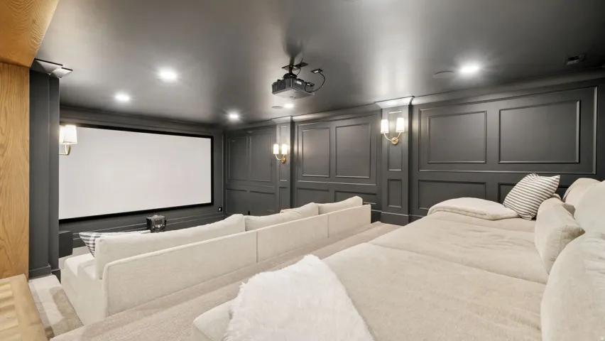 Dedicated home theater featuring a large projection screen, ceiling-mounted projector, recessed lighting, and panel-molding wall accents