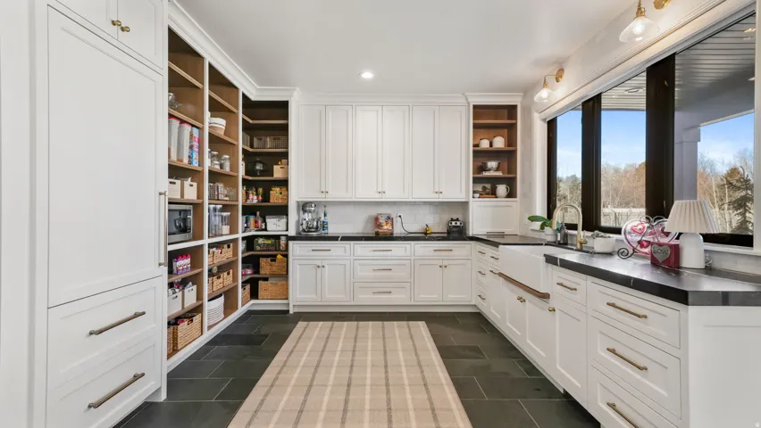 Spacious kitchen featuring white cabinetry, dark countertops, a farmhouse sink, and a full wall of built-in shelving