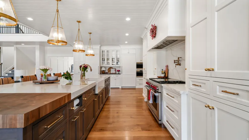 Gourmet kitchen featuring a large central island with integrated sink, two-tone cabinetry, professional-grade stainless steel range, built-in ovens, and hardwood flooring