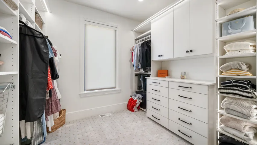 Custom closet system featuring white cabinetry, integrated shelving, and undermount lighting