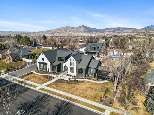 Contemporary home featuring a light-colored stone and dark siding exterior, dark shingle roofing, a paved driveway, and mature landscaping