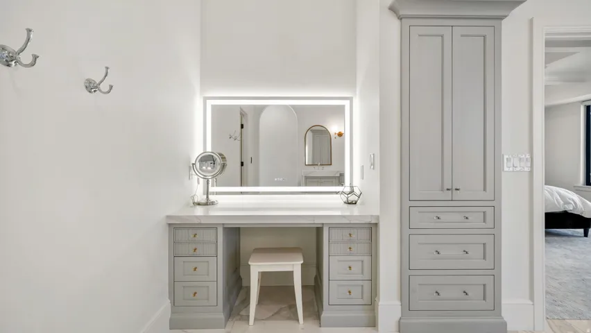 Vanity area featuring a backlit mirror, stone countertop, gray cabinetry with brass hardware, and built-in storage tower