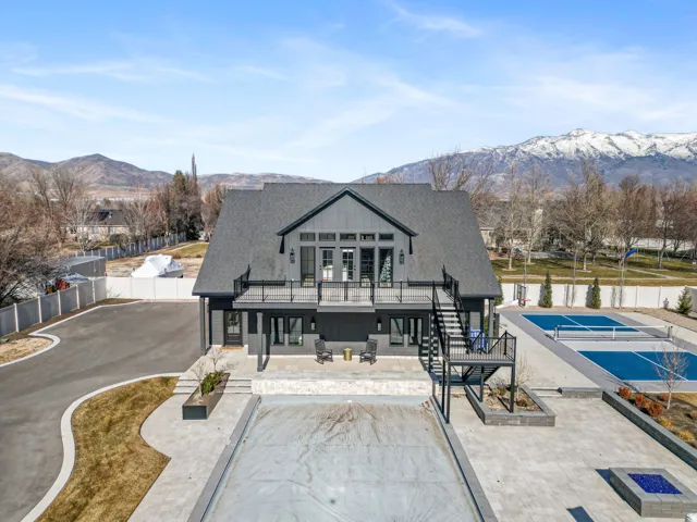 Contemporary two-story residence featuring a dark gray facade, expansive rear patio, upper-level balcony with black railings, and an integrated outdoor fire pit