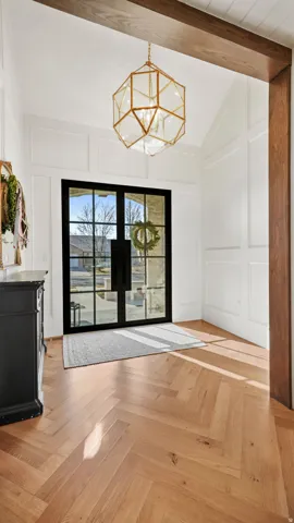 Grand entryway featuring herringbone wood-finish flooring, white paneled walls, and a vaulted ceiling with exposed wood beams