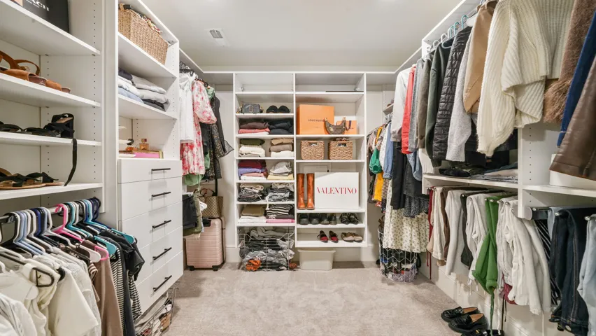 Expansive closet featuring abundant white built-in shelving, multiple hanging rods, integrated drawers with dark hardware, and recessed overhead lighting