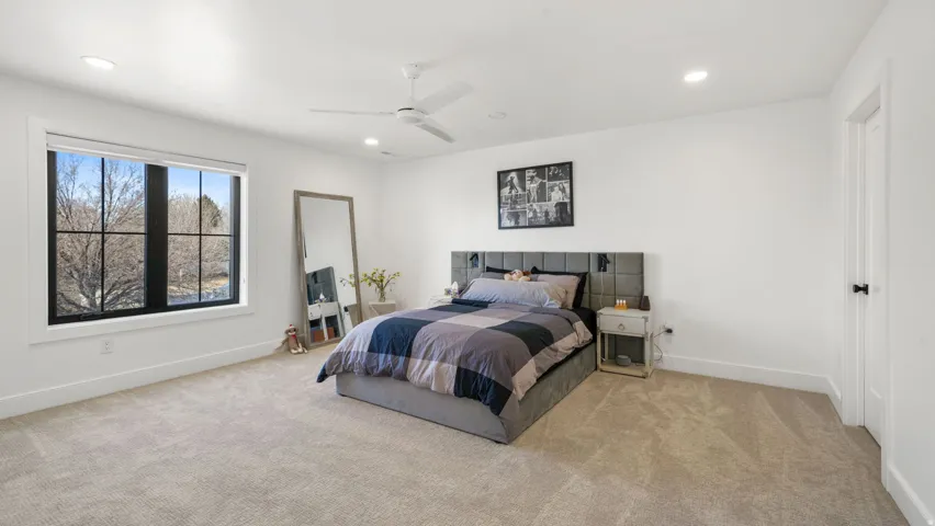 Spacious room featuring neutral carpeting, a large window with black framing, recessed lighting, and a ceiling fan