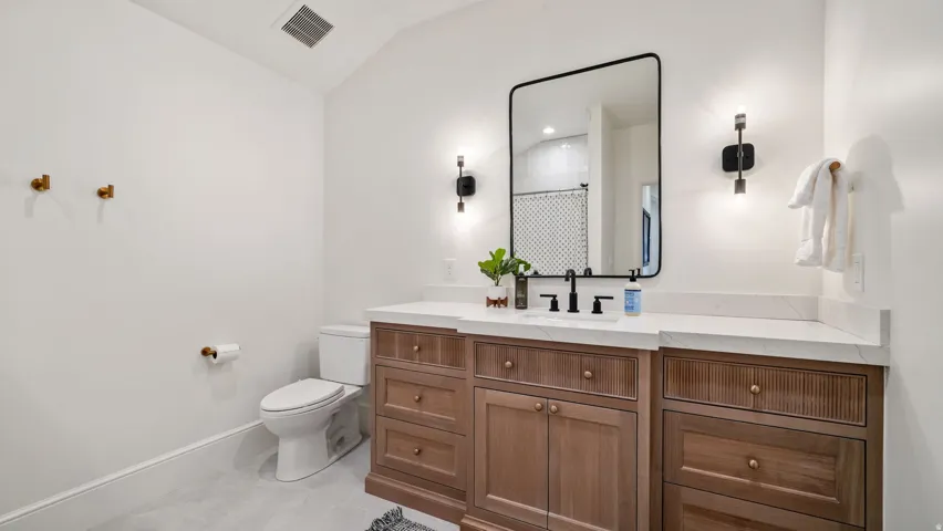 Bathroom featuring a light wood-finish vanity with a single sink and matte black faucet, a large rectangular mirror, and white countertops
