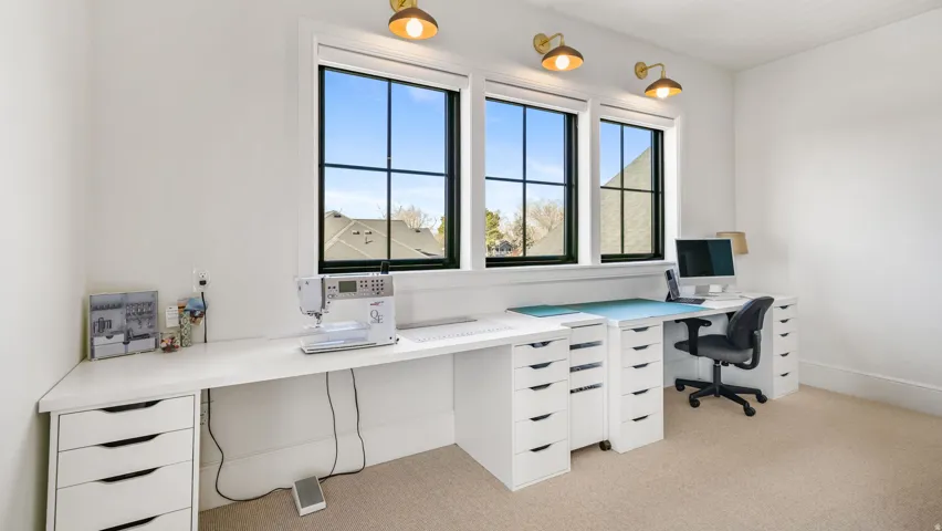 Bright room featuring three large windows with black grilles, integrated wall sconces, extensive built-in white countertops, and multiple storage drawers