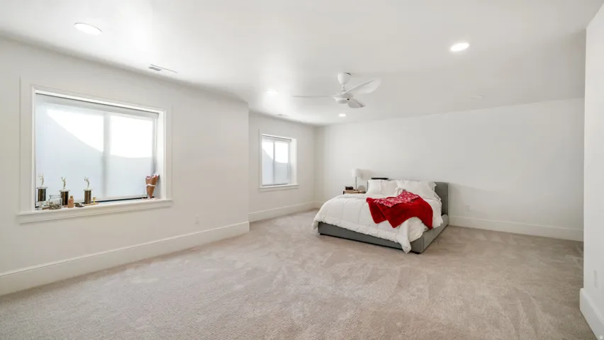 Spacious room featuring light-colored carpeting, recessed lighting, a modern ceiling fan, and multiple windows with white trim