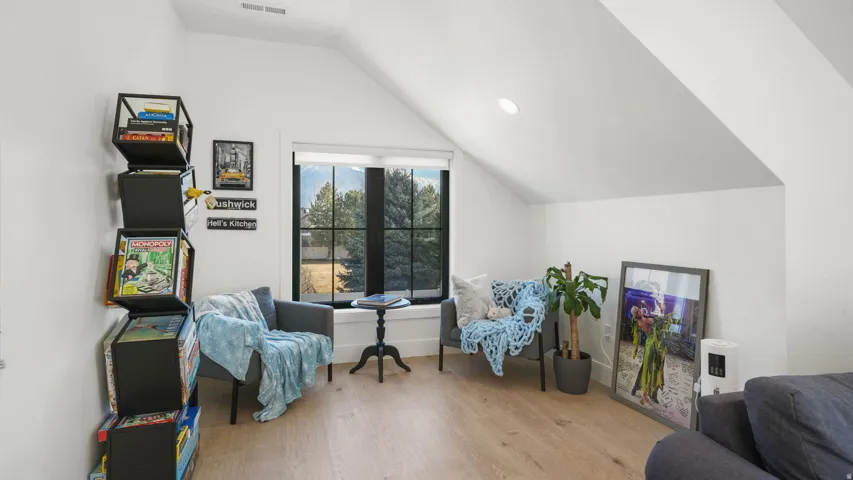 Attic space featuring wood-finish flooring, a vaulted ceiling, and a large window with black framing