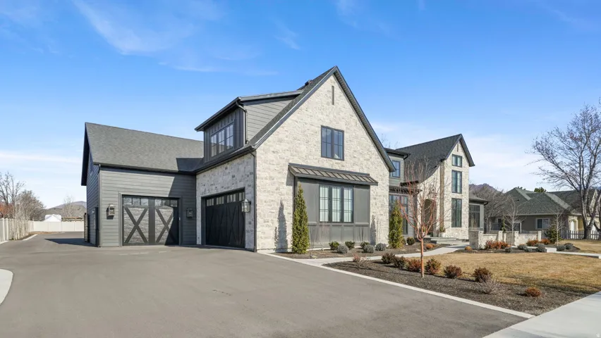 Stone and siding exterior featuring a multi-car garage with carriage-style doors, an asphalt driveway, and mature landscaping