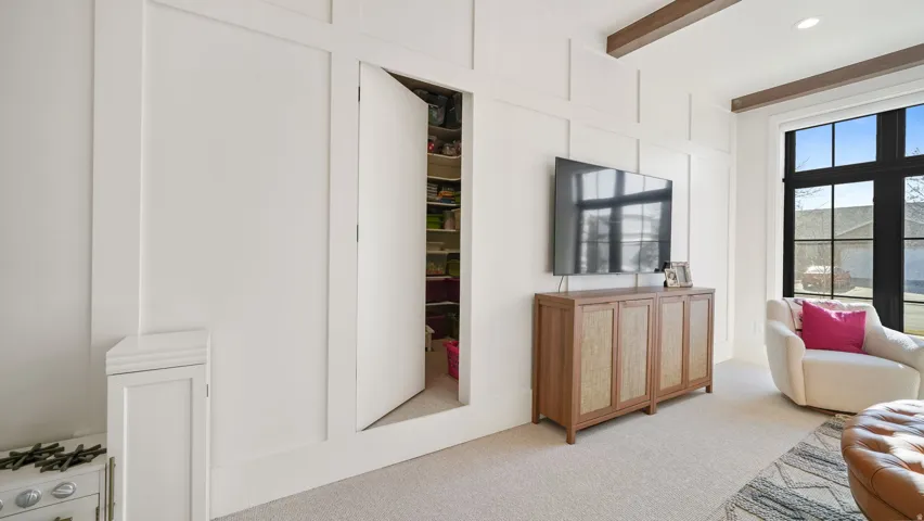 Recessed storage area with shelving, paneled walls, high ceilings with exposed beams, and a large window featuring dark-framed panes