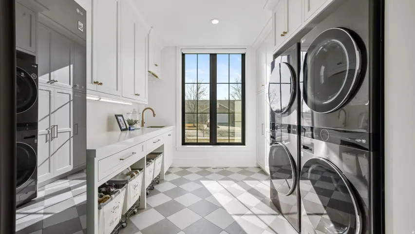Dedicated laundry room featuring white cabinetry, a built-in sink with a brass faucet, and checkerboard floor tiling