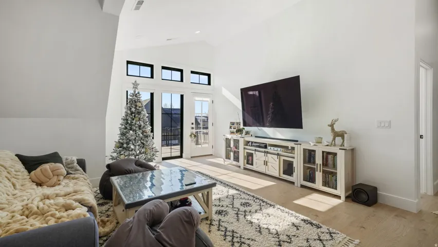 Vaulted ceiling living space featuring light wood-finish flooring, white walls, and a multi-panel glass door with transom windows