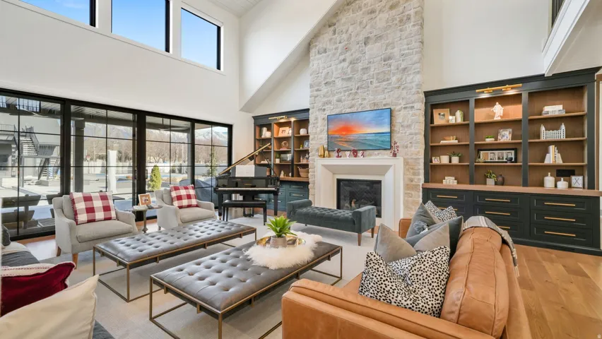 Vaulted ceiling living area featuring a stone accent wall with fireplace, built-in shelving, hardwood flooring, and large windows with black frames