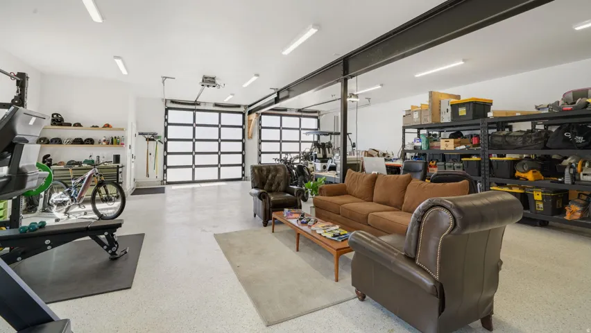 Spacious garage featuring two glass-paneled sectional doors, polished concrete flooring, exposed structural beams, and ample shelving for storage