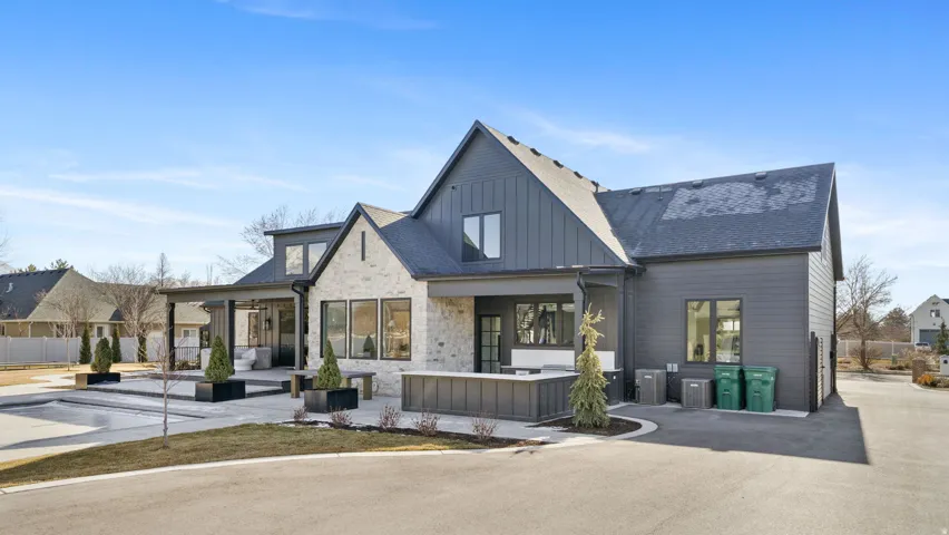 Modern farmhouse exterior featuring a light stone facade, dark vertical siding, and a dark shingle roof