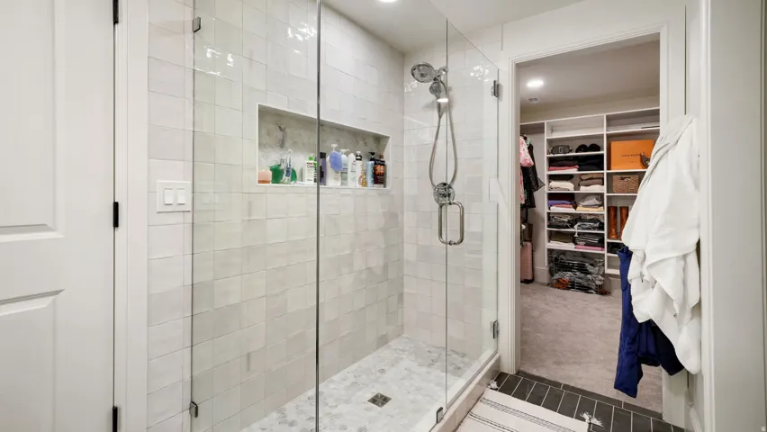 Glass-enclosed shower with subway tile surround, recessed niche, and stone mosaic flooring