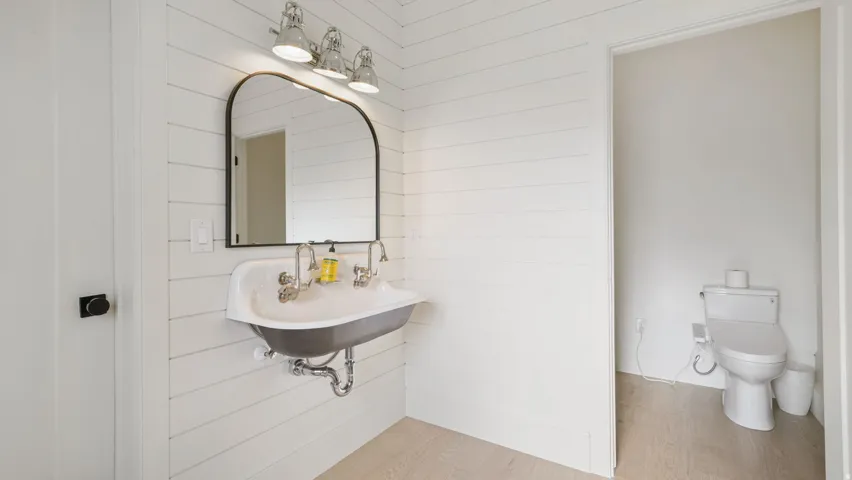 White shiplap walls complement a wall-mounted basin sink with dual faucets and a black-framed mirror