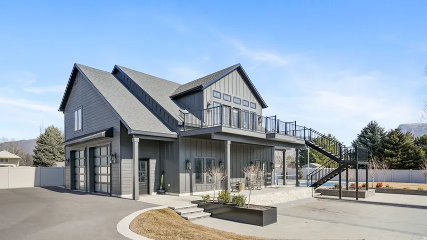Contemporary property featuring a gray board and batten exterior, expansive upper-level deck with metal railings, external staircase, and a two-car garage with glass panel doors