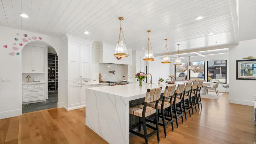 Spacious kitchen featuring an oversized island with countertop seating, white shaker cabinetry, wood-finish flooring, and shiplap ceilings