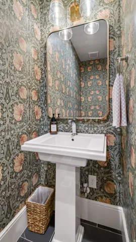 Pedestal sink with polished chrome faucet, set against patterned wallpaper