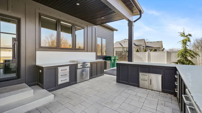 Outdoor kitchen featuring built-in stainless steel appliances, dark cabinetry, and light countertops, set on a paver patio