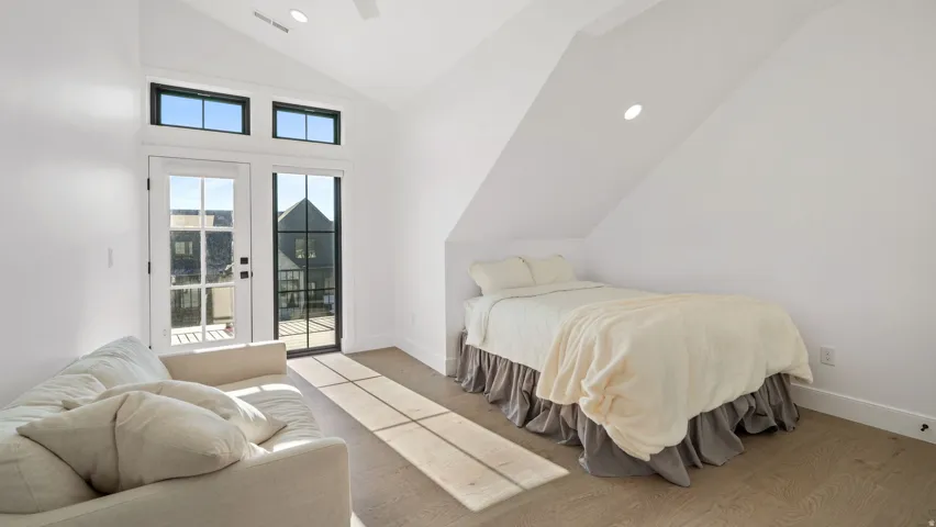 Vaulted ceiling room with wood-finish flooring, featuring a glass-paned door to the exterior, transom windows, and recessed lighting