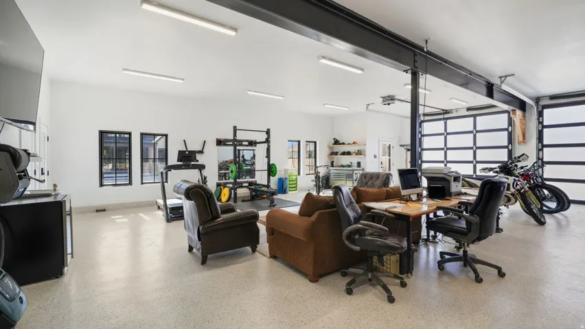 Spacious multi-functional room with white walls, three transom windows, exposed structural beams, and two glass-paneled garage doors