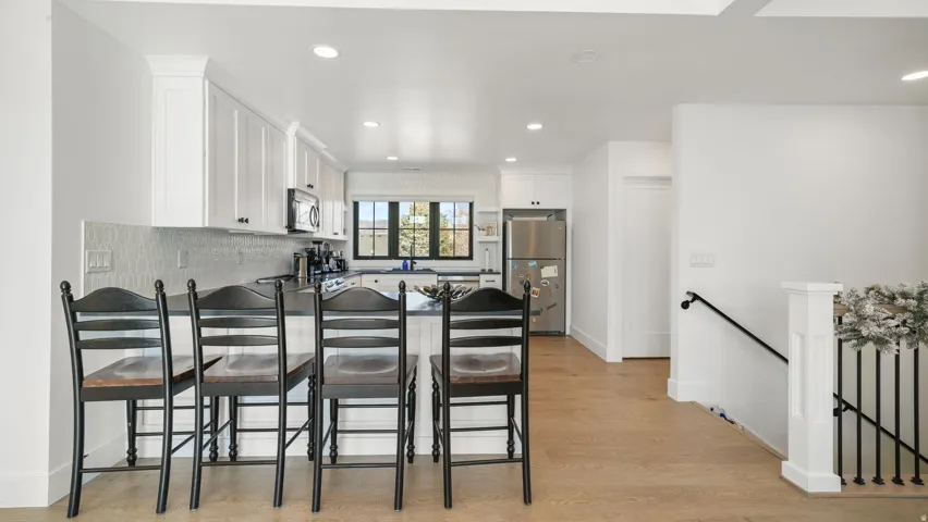 Modern kitchen featuring white cabinetry, stainless steel appliances, a patterned backsplash, and an integrated breakfast bar
