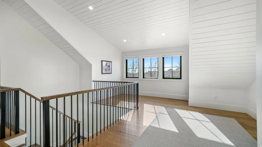 Upper level landing featuring wood-finish flooring, white shiplap ceiling details, and black iron balusters with wood handrails