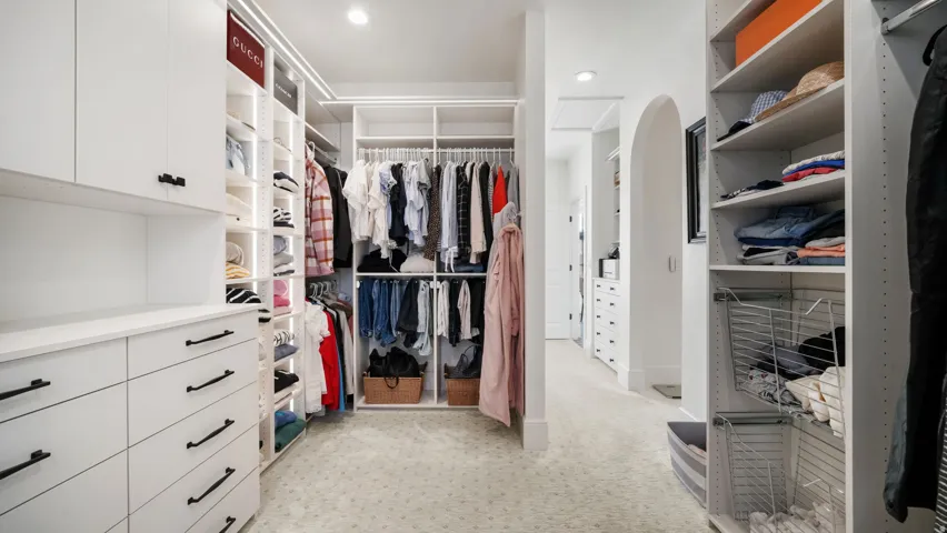 Spacious walk-in closet featuring custom white cabinetry with black hardware, recessed lighting, varied shelving, and integrated hanging rods