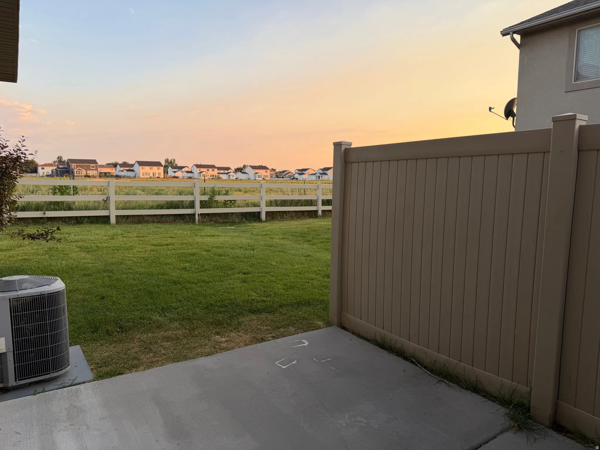 Expansive backyard featuring a green lawn, concrete patio, and a light brown privacy fence